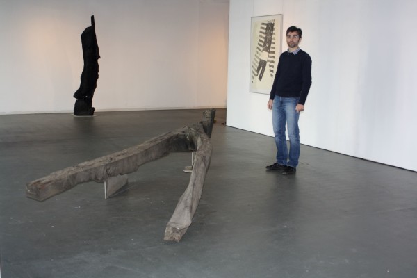 Kustos Alexander Stoll, umgeben von Exponaten der Ausstellung:  vorn eine „Barriere“ genannte liegende Figur, dahinter  der aus schwarzer Eiche geschaffene „Ecce homo“ als  geschundener Mensch und an der Wand ein Holzdruck