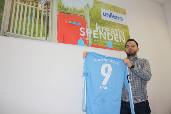 Vizepräsident Rico Bach von dem verein unikero präsentiert das unterschriebene Trikot von dem Chemnitzer Fußballspieler Anton Fink.