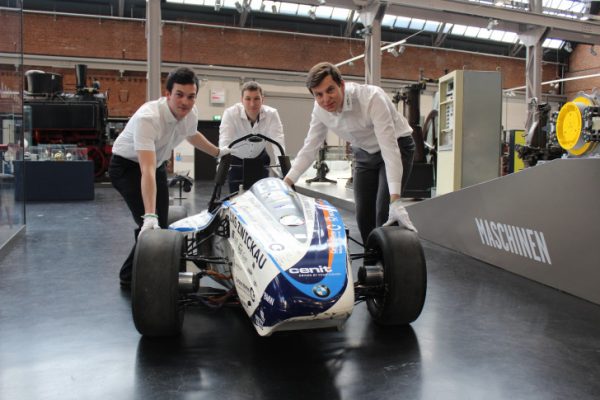 Die Studenten der Westsächsischen Hochschule Zwickau, Maximilian Pöhlmann, Thomas Ganzer, und Projektleiter Manuel Seifert (v.li.) fahren den Rennwagen „eGon“ zum Podium, auf dem der Elektrorennwagen ausgestellt wird. Foto: Nicole Neubert